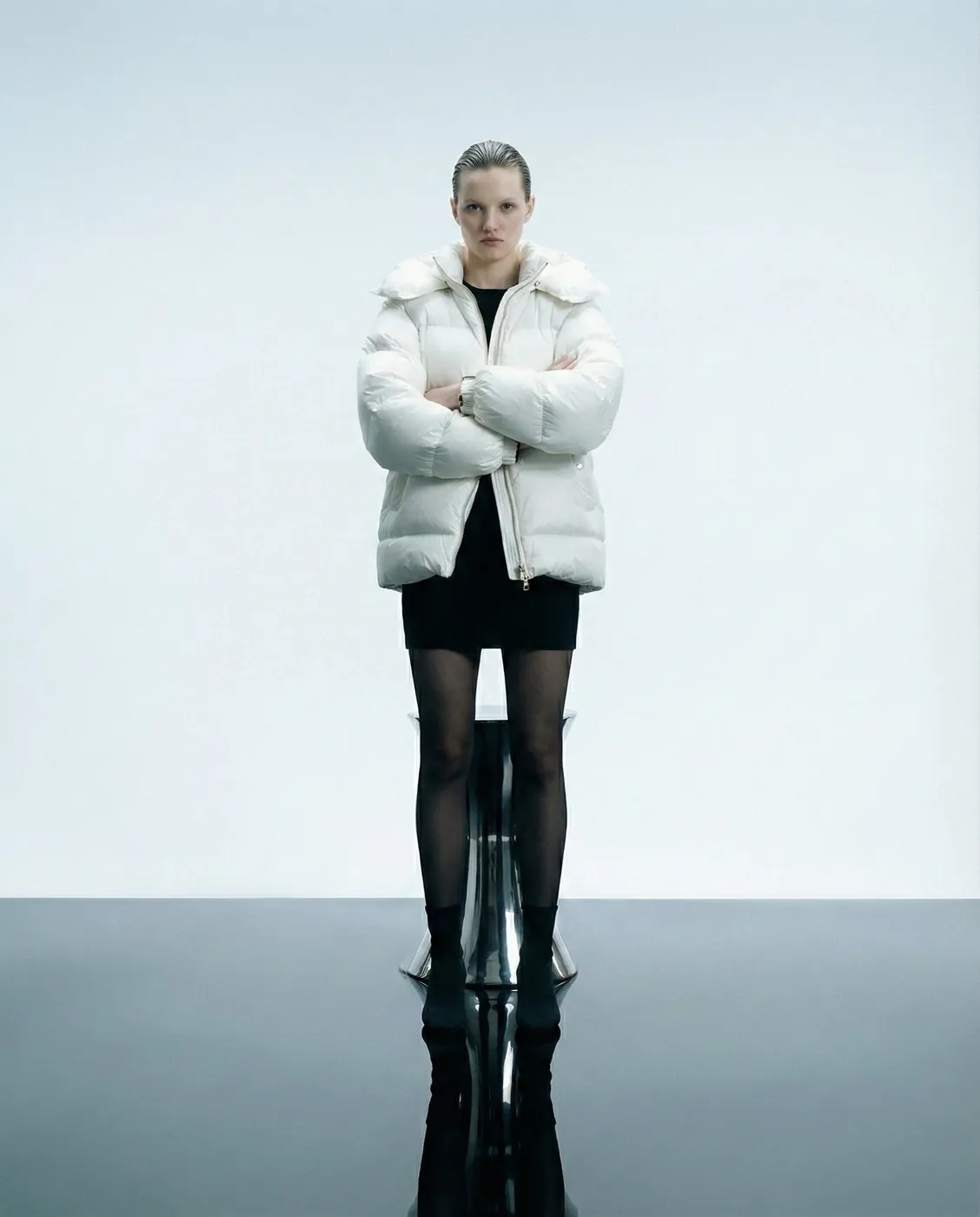 A model in a white puffer jacket on a mirror-still floor
