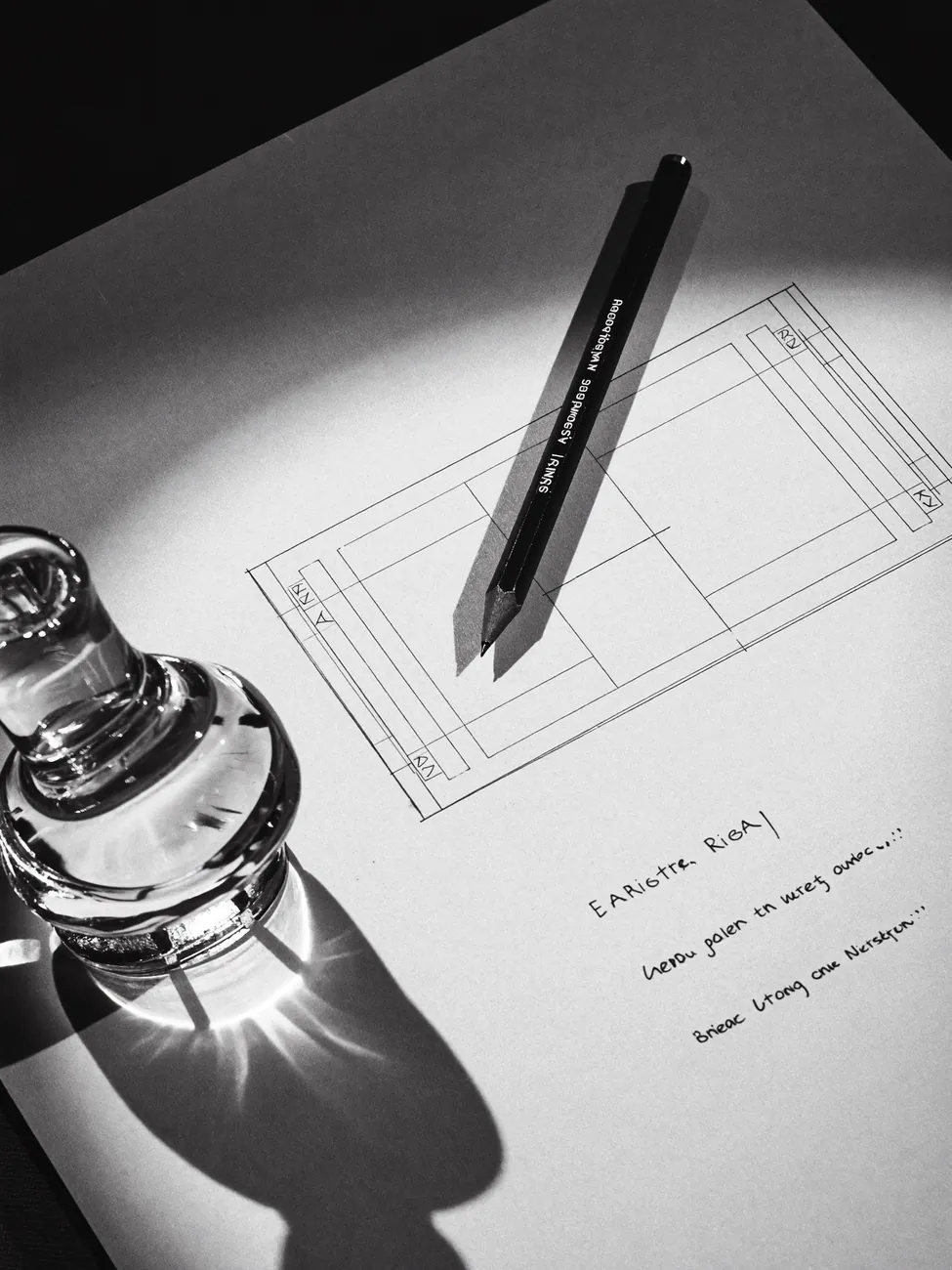 A pen resting on a hand-drawn layout sketch beside a glass object