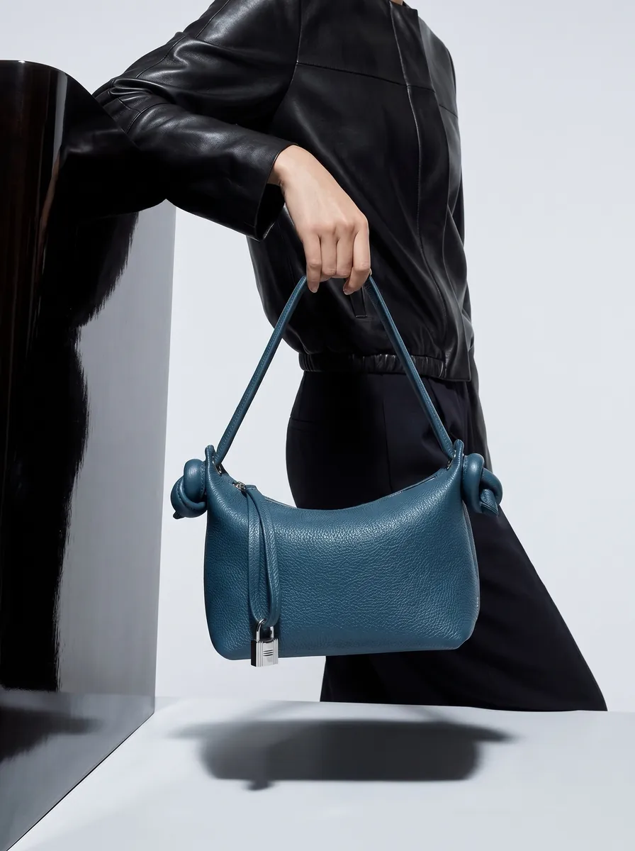 A blue leather bag held out from a black coat